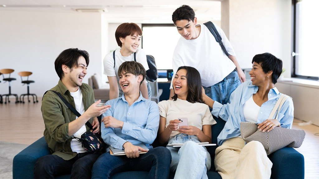 Một nhóm sinh viên ngồi trò chuyện và cười đùa vui vẻ trong không gian học tập hiện đại, thể hiện sự gắn kết và năng lượng tích cực.